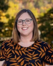 headshot photo of professor Sumer Musick, wearing an orange and black top, background is autumn at UPIKE