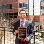 KYCOM student Mustafa Basree stands on campus holding his award for preventive medicine writing.