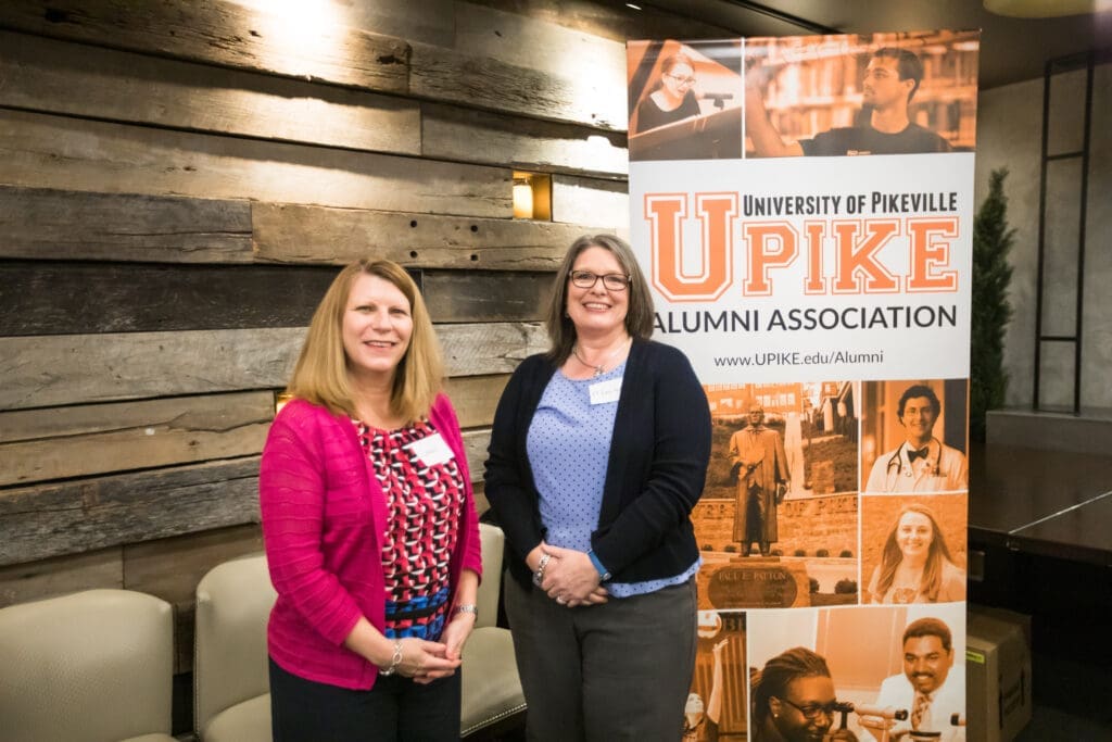 Two ladies pose in front of UPIKE banner