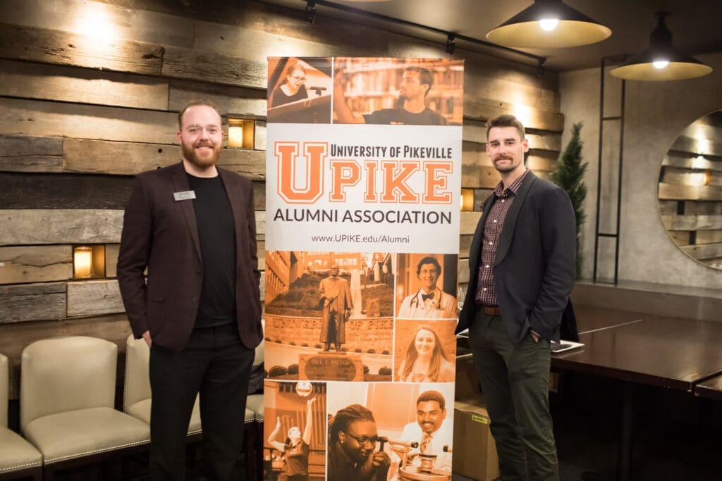 two guests pose for a photo in front of UPIKE banner