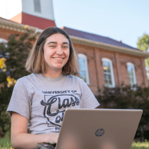 Student sitting in front of the Academy Building with a laptop
