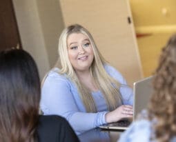 student working on laptop talking to other students