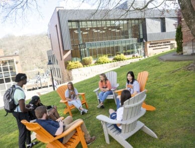 students sitting in chairs outside of dorm on campus