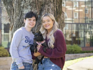 two students posing on campus with their dog.