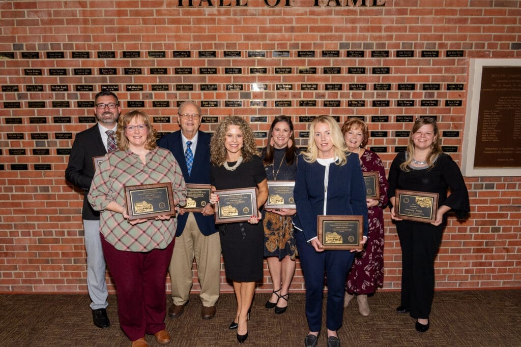 Distinguished Educators standing in front of the wall with name plaques of past inductees.