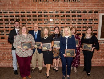 Distinguished Educators standing in front of the wall with name plaques of past inductees.