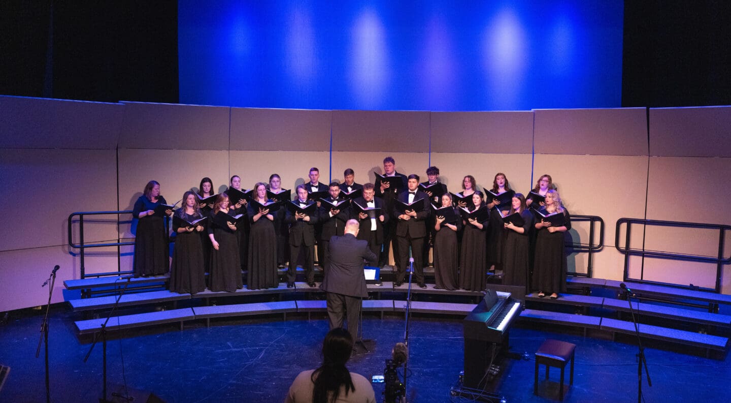 Choir singing with music sheet books and lit with blue and white lighting