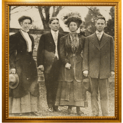 Sepia-toned historic photograph of two men and two women in early 1900s attire, framed in a decorative gold frame.