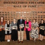 Inductees holding their plaques in front of the hall of fame wall.