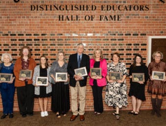Inductees holding their plaques in front of the hall of fame wall.