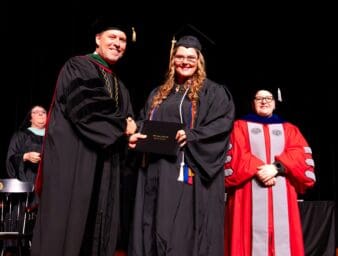 New graduate, Haley McKinney accepting her diploma from UPIKE President Burton Webb