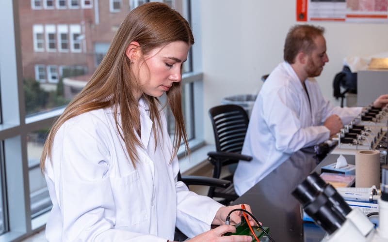 Two researchers in lab coats concentrate on lab tasks near microscopes and scientific tools.