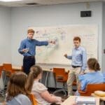 Students in front of class explaining content on a white board