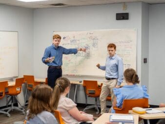 Students in front of class explaining content on a white board