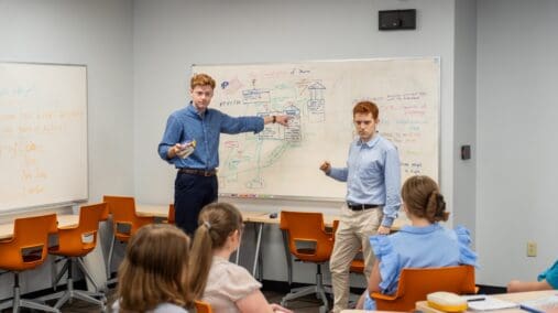 Students in front of class explaining content on a white board