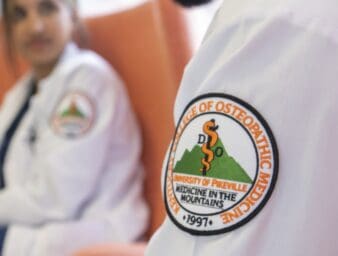 Close-up photo of the KYCOM patch on a white lab coat.