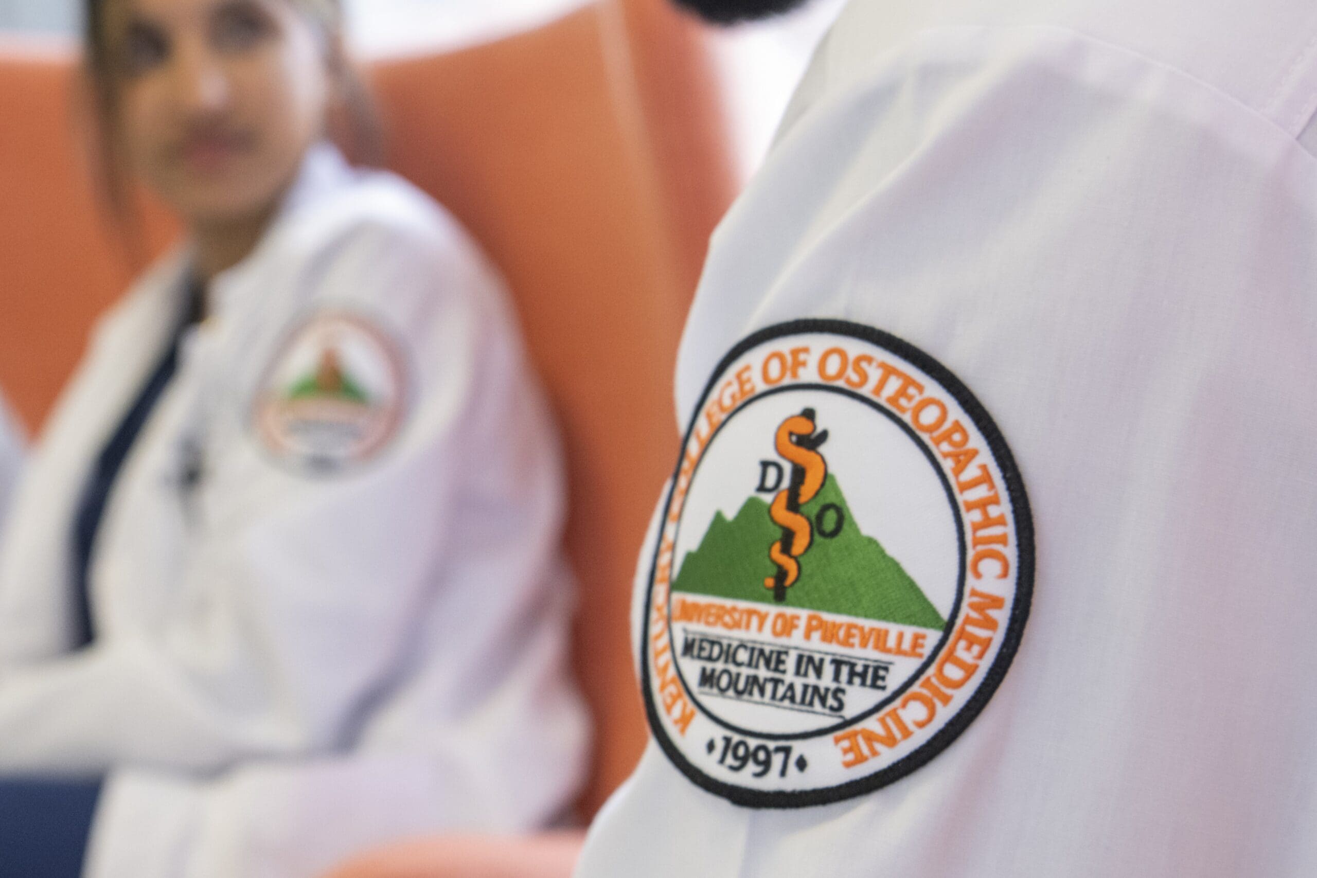 Close-up photo of the KYCOM patch on a white lab coat.