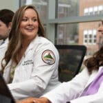 Two female KYCOM students having a conversation in front of a laptop.