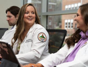 Two female KYCOM students having a conversation in front of a laptop.