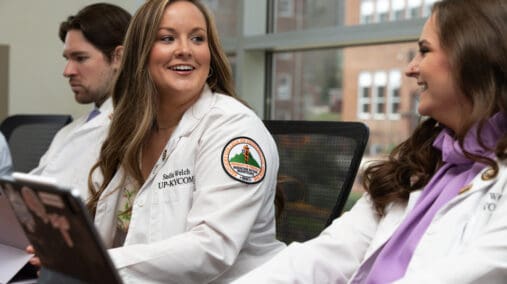 Two female KYCOM students having a conversation in front of a laptop.